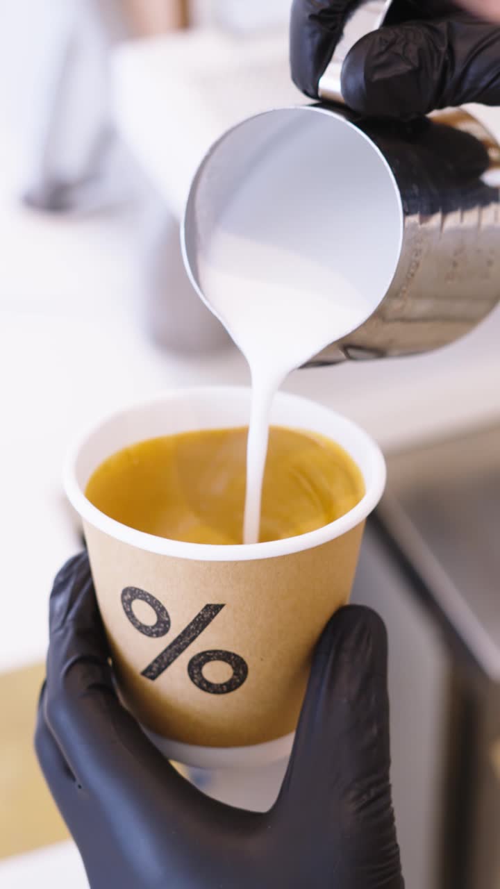 A barista pouring milk into a branded Arabica cup
