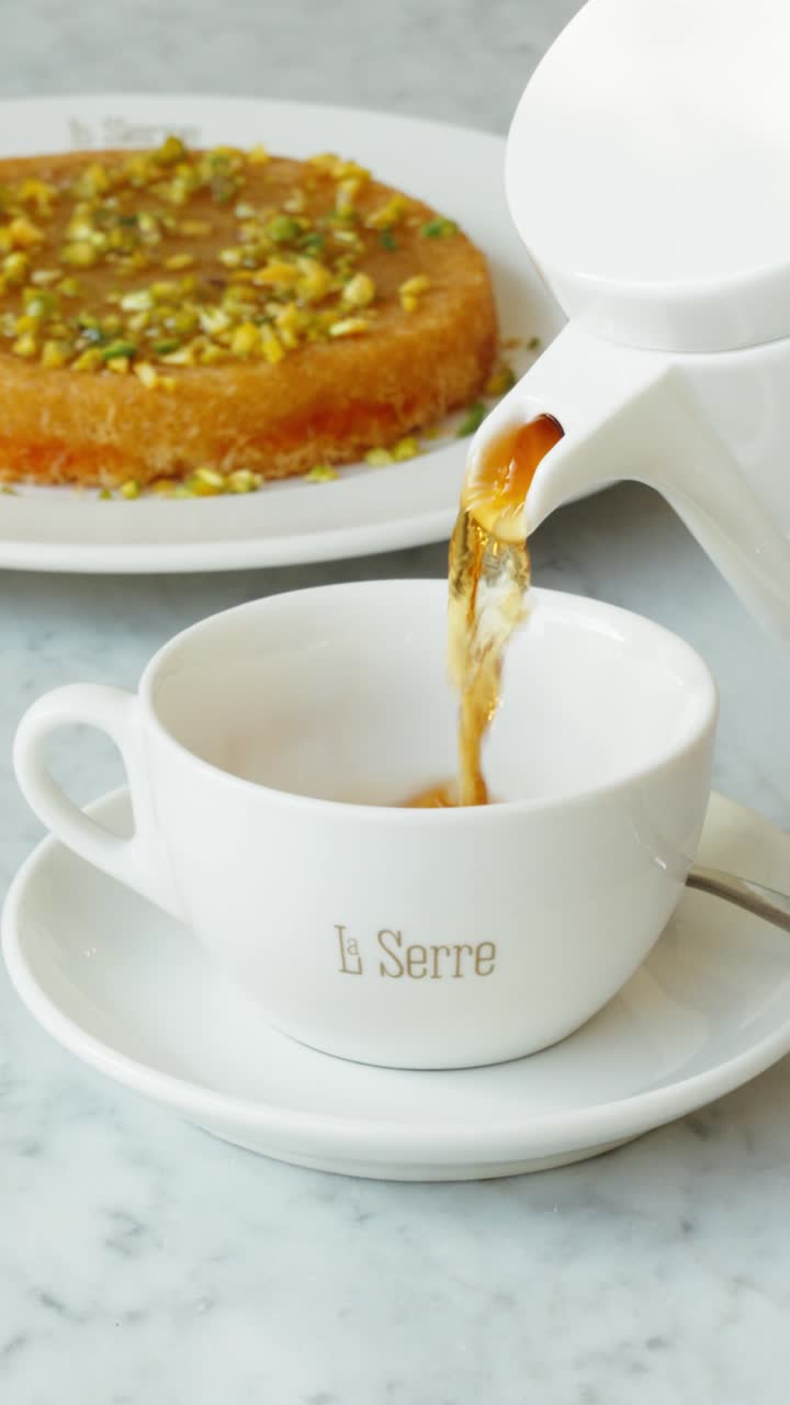 Tea poured beside a pistachio kunafa cake on white marble