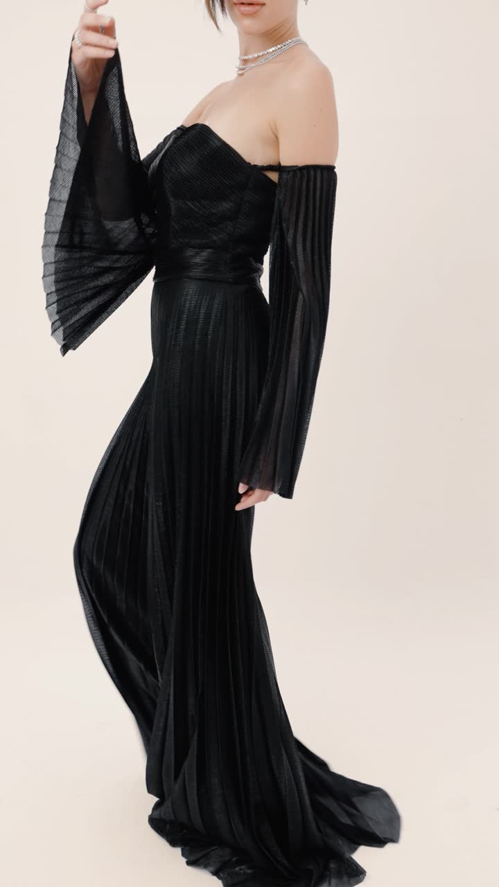 A model in a black pleated gown against a cream studio backdrop