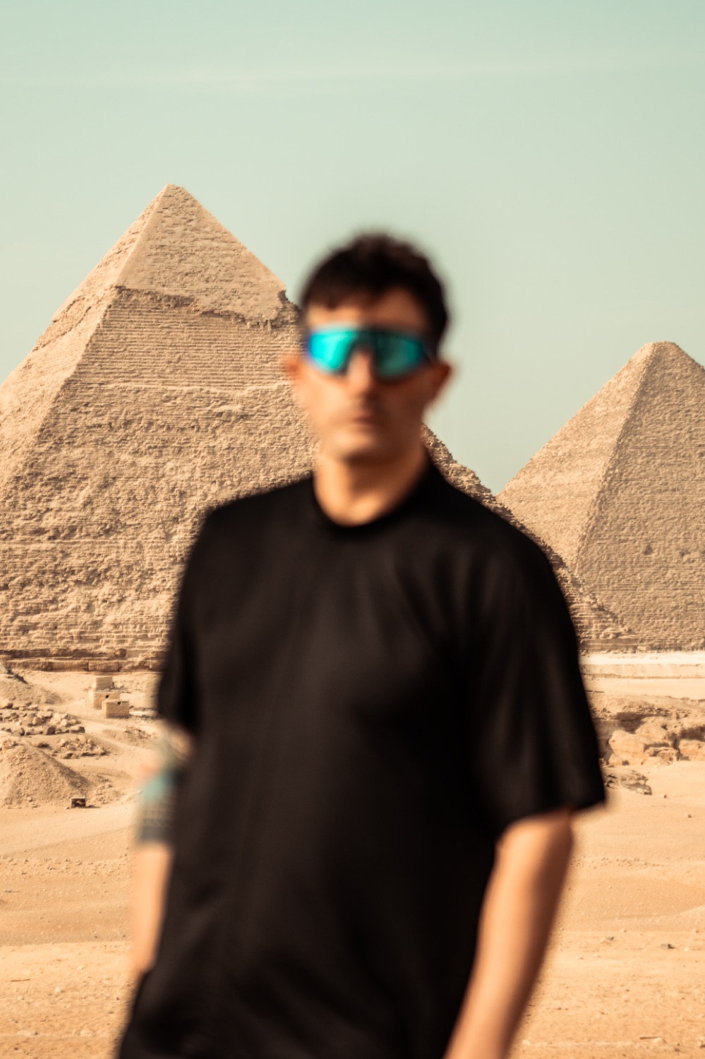 A man at the pyramids of Giza, sunglasses mirroring the stone