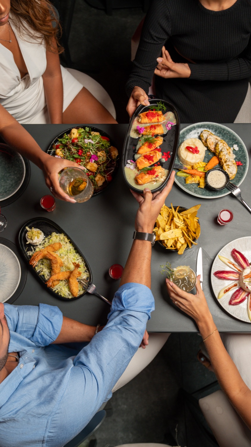 A shared table shot from above, hands reaching for plates