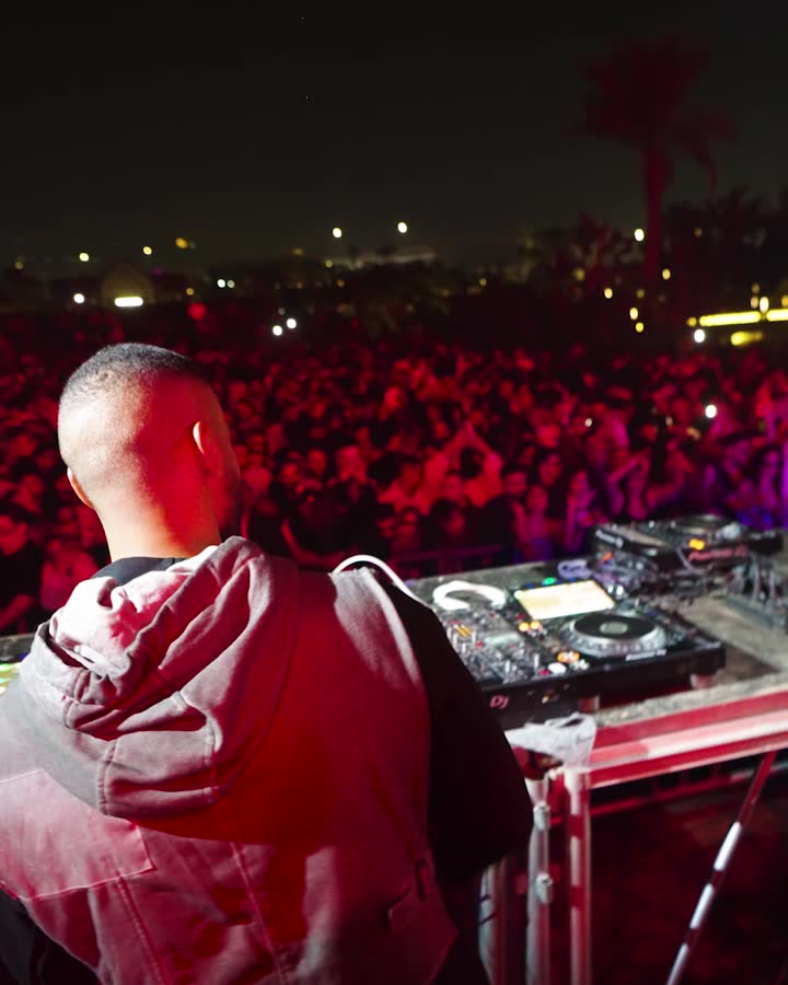 A hooded DJ before a red-lit festival stage